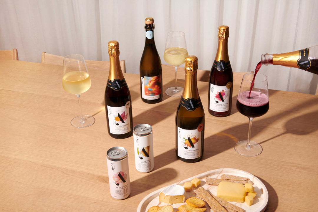 Altina non-alcoholic sparkling wines displayed with bottles and cans on a table, two filled glasses, a drink being poured, and cheese and crackers for pairing