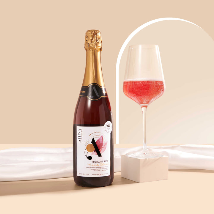 Altina sparkling rosé bottle beside a stemmed glass filled with pink sparkling wine, the glass raised on a small cream block, set on a beige surface with draped white fabric and a soft arched backdrop